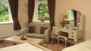 A room with a sofa, a small table, a dresser with a mirror, and a window with curtains.