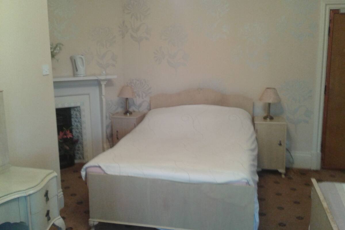 A bedroom with a bed, two bedside tables, a nightstand, a dresser, and a wall with floral wallpaper.
