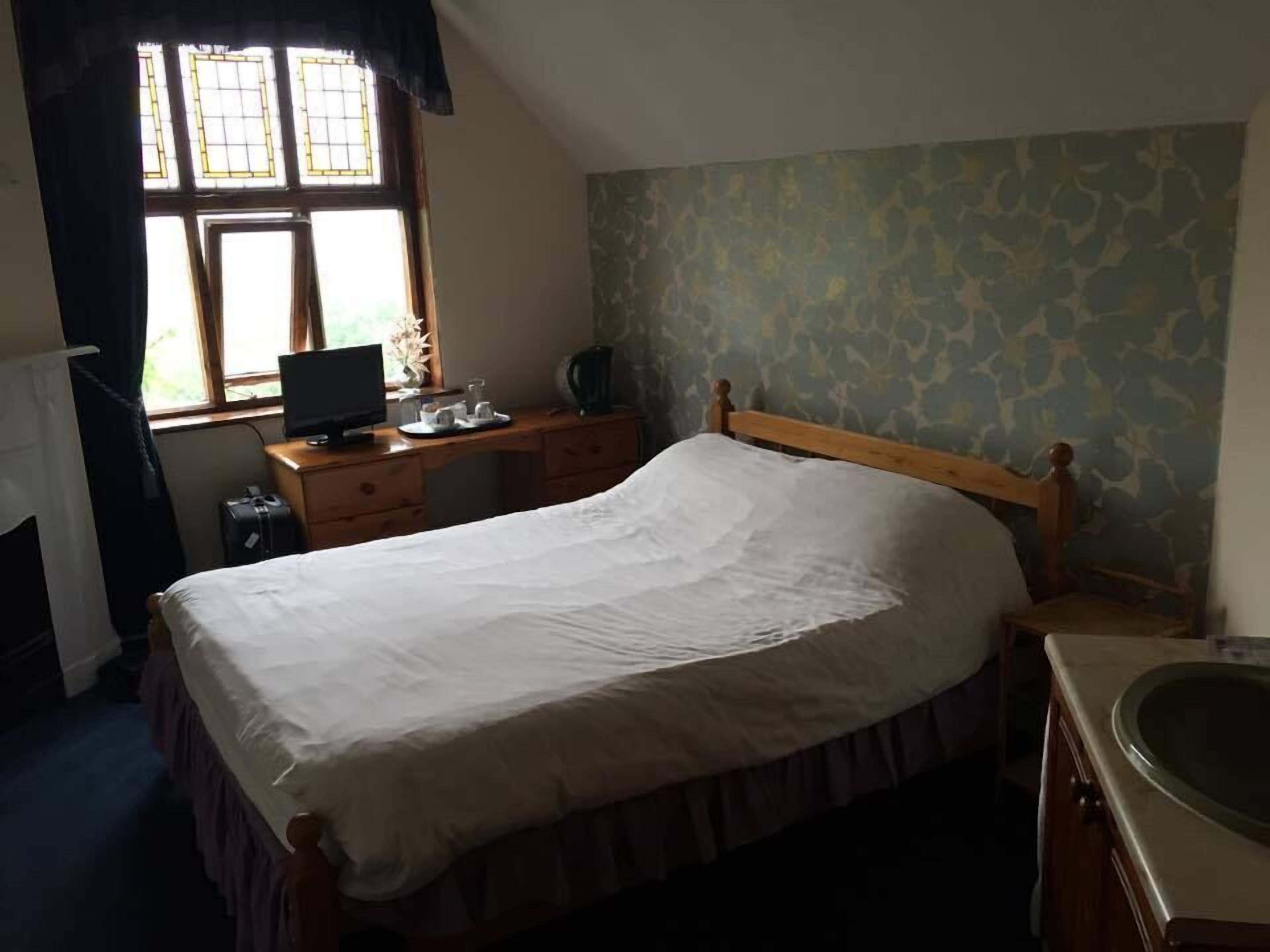 A bedroom with a bed, a desk with a computer, a window, and a bathroom.