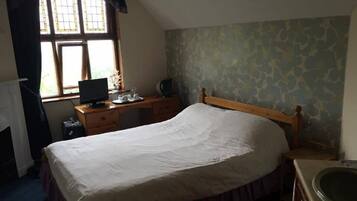 A bedroom with a bed, a desk with a computer, a window, and a bathroom.
