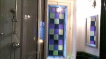 Un baño con ducha, lavamanos y ventana con un colorido diseño acolchado.
