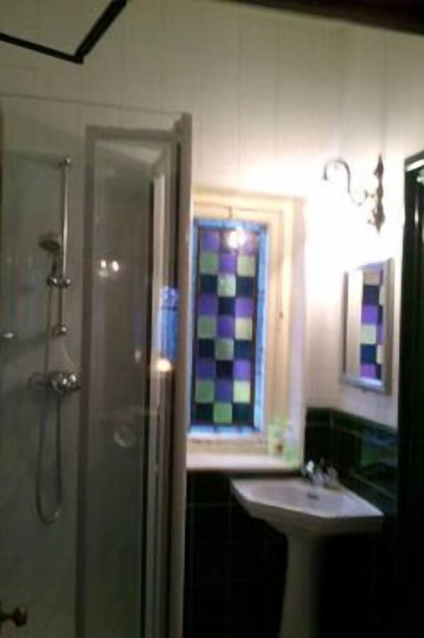 Un baño con ducha, lavamanos y ventana con un colorido diseño acolchado.