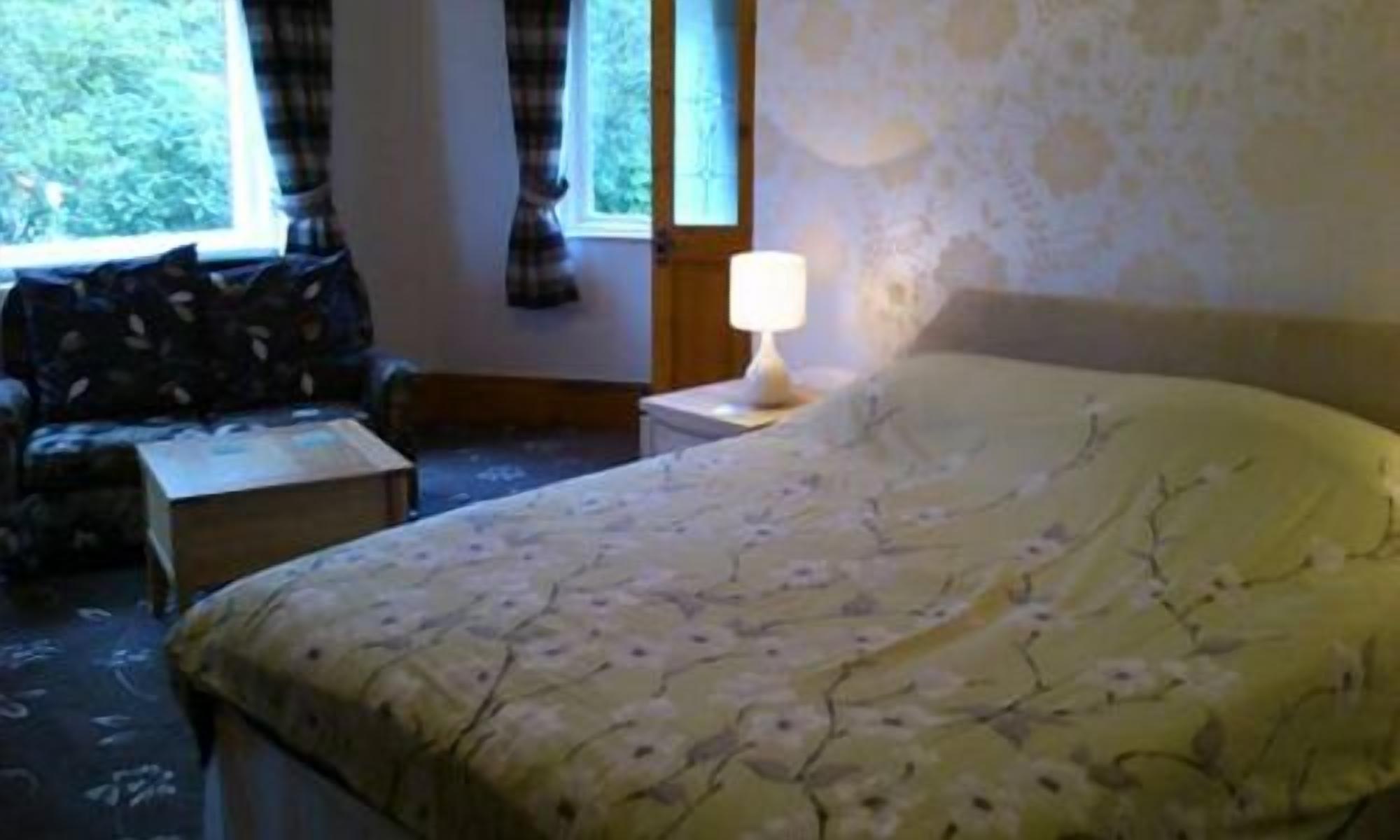 A bedroom with a bed, a nightstand, a lamp, a window with curtains, and a small table.