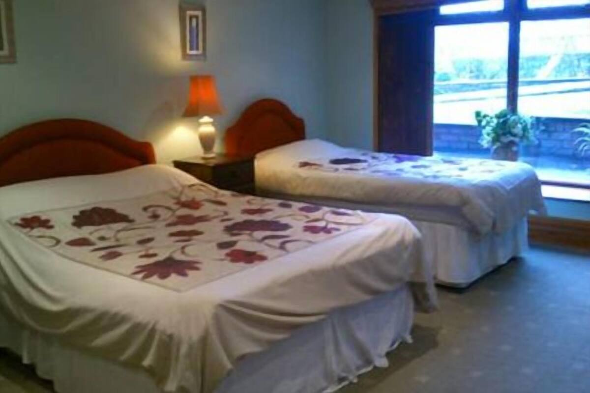 A hotel room with two beds, each with a floral bedspread, a nightstand with a lamp, and a window with a view of greenery.