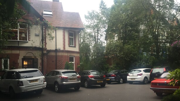 A parking area with several cars parked in front of a building with a brick facade and a tiled roof.