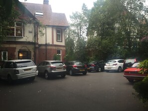 Un área de estacionamiento con varios coches aparcados frente a un edificio de fachada de ladrillo y techo de tejas.