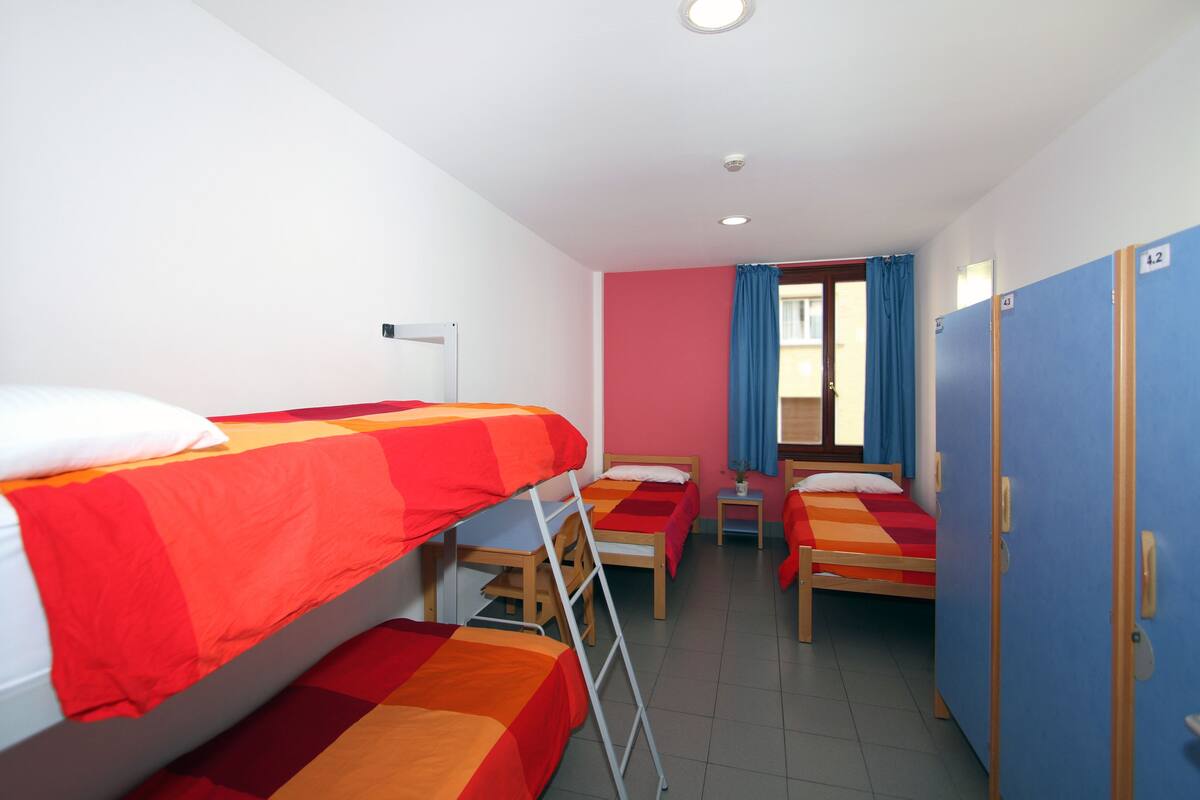 A dormitory room with bunk beds, a desk, and a wardrobe.