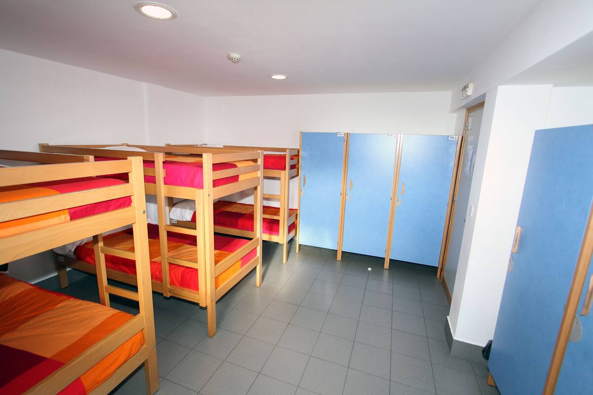 A dormitory room with bunk beds, a wardrobe, and a door.