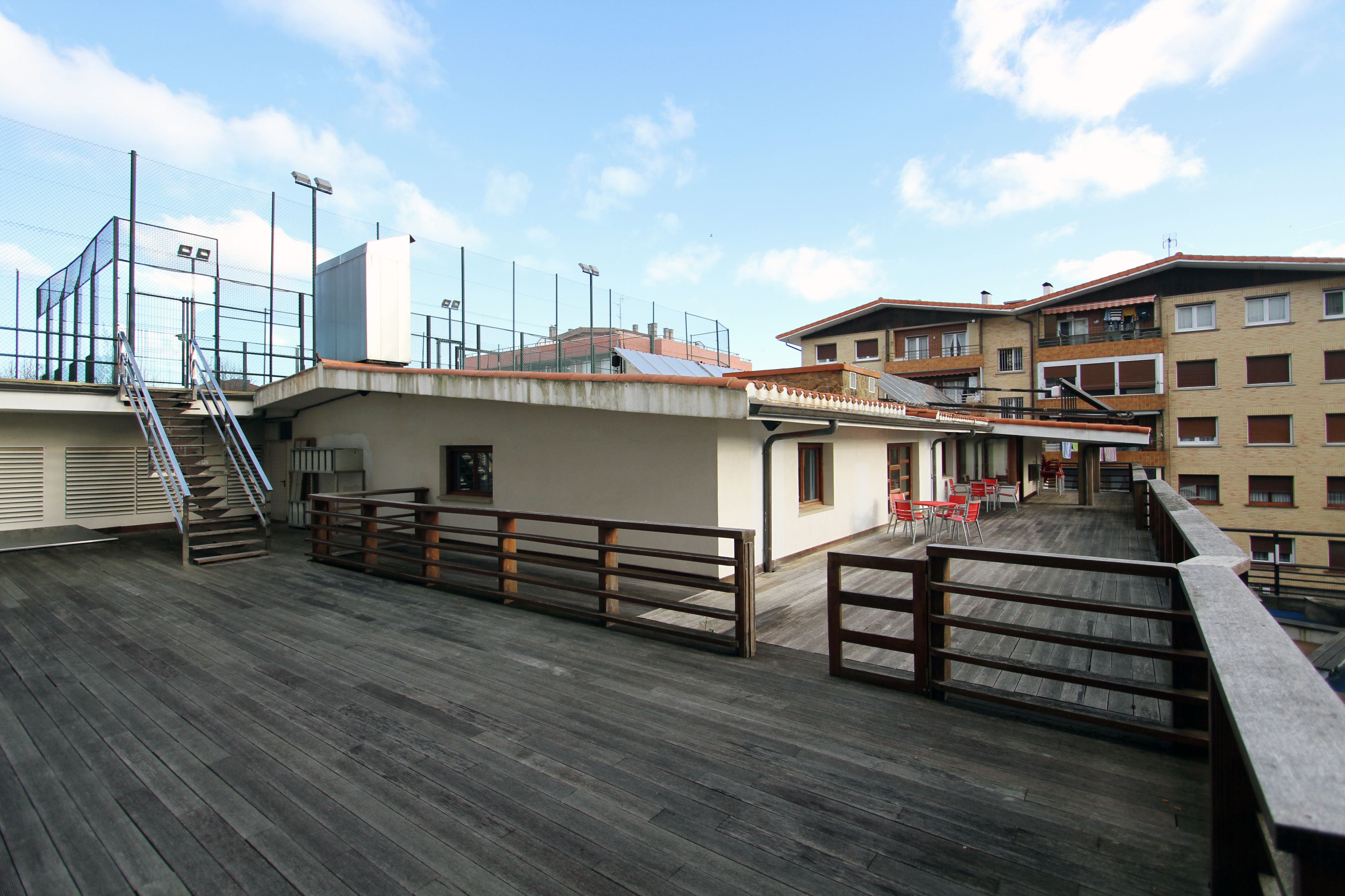 A wooden deck with a railing, a staircase, and a building with multiple windows and balconies.