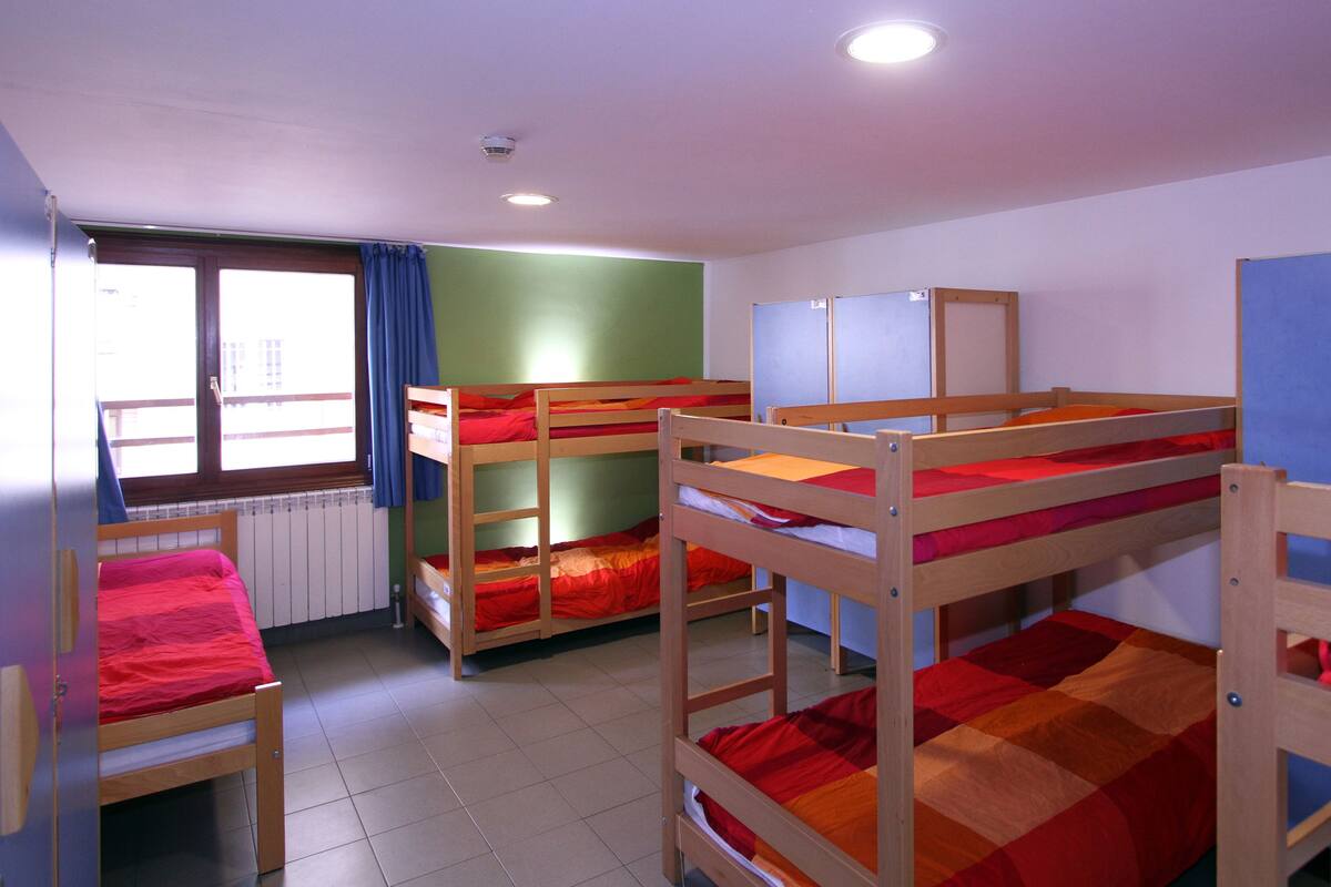 A dormitory room with bunk beds, a window with curtains, and a radiator.