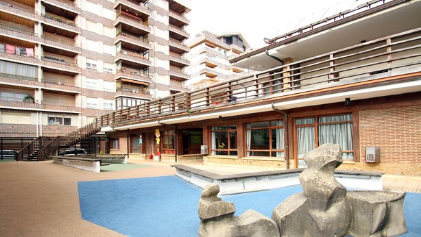 A multi-story building with balconies, a blue outdoor area with a sculpture, and a staircase leading to the upper floors.