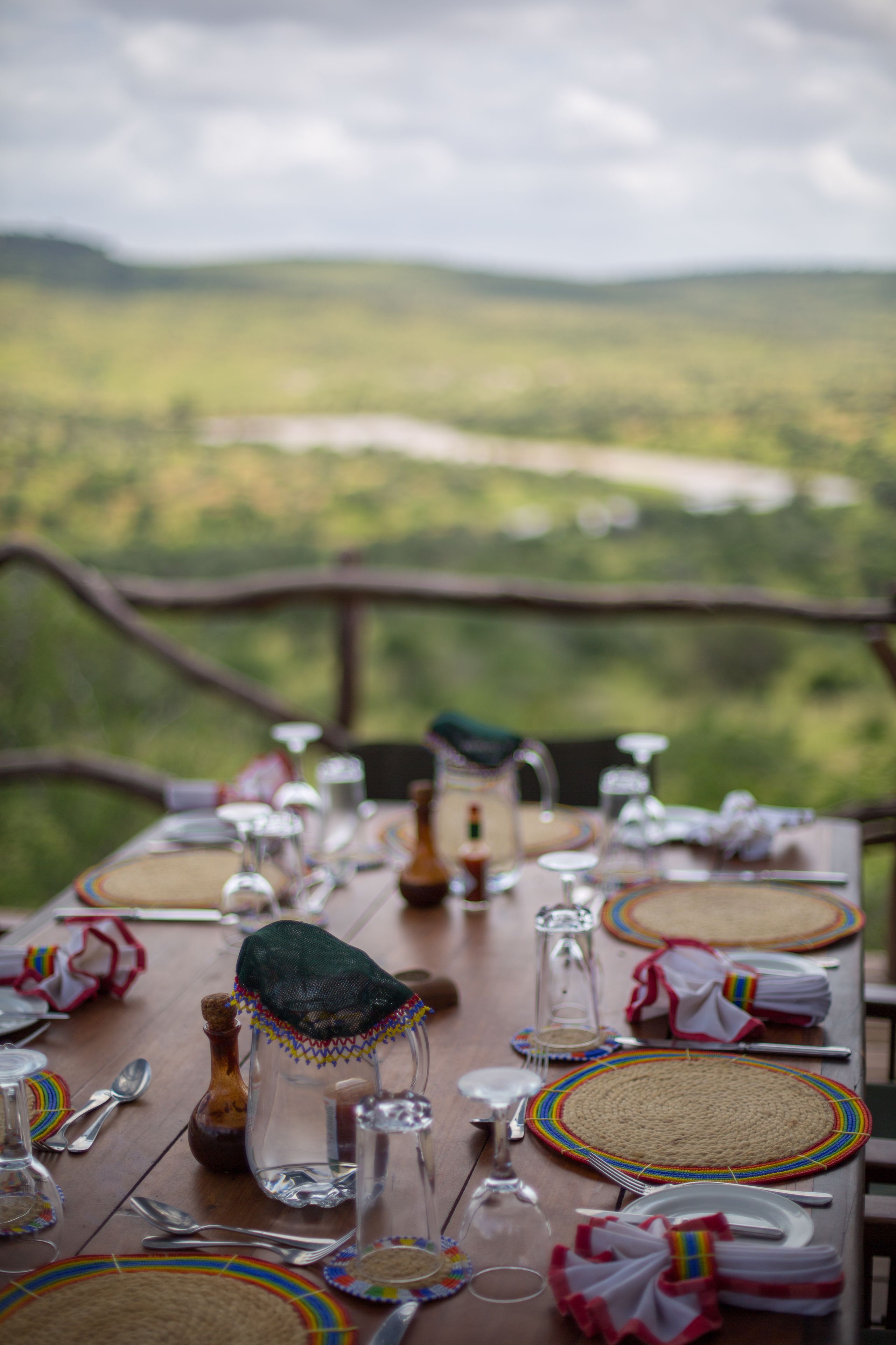 A dining table set with plates, glasses, and cutlery, overlooking a scenic landscape.