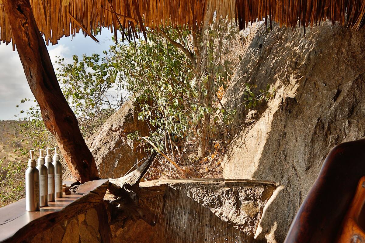 A rustic bathroom with a thatched roof, a wooden bench, and a stone sink.