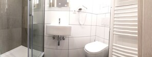A modern bathroom with a glass shower enclosure, a white sink, and a toilet. - Hotel Kriemhilde (Worms)