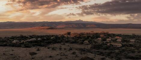 A landscape with a village of thatched-roof houses, a mountain range, and a sunset sky.