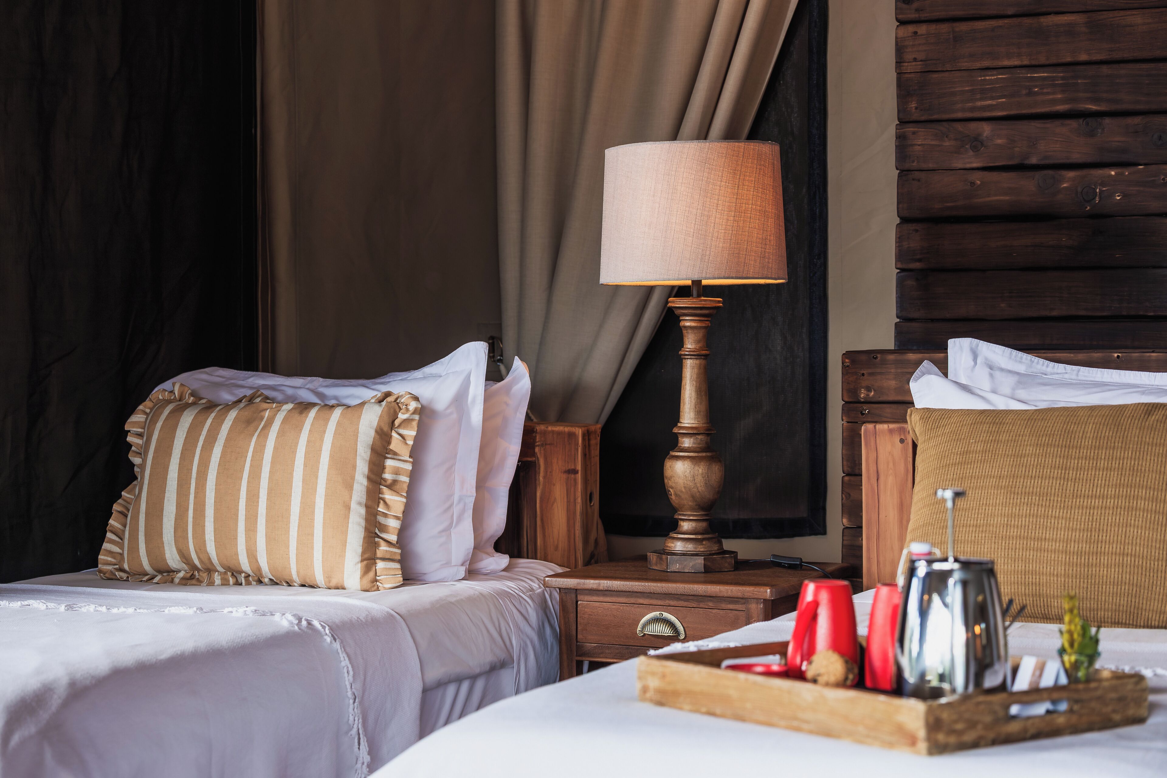 Een hotelkamer met twee bedden, een houten nachtkastje, een lamp en een dienblad met spullen.
