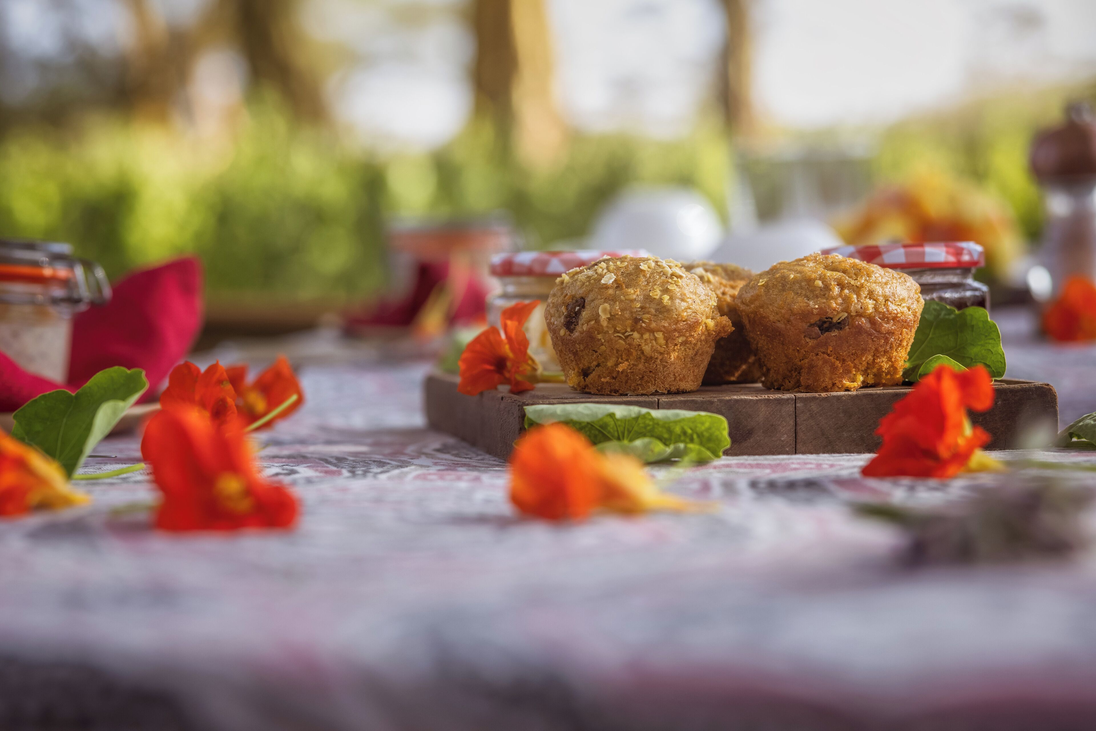 Dos muffins sobre una tabla de madera con flores rojas y hojas verdes en una mesa.