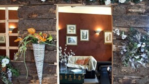Een rustieke kamer met een houten wand, een groene dressoir, een witte vaas met bloemen en ingelijste foto's aan de muur.