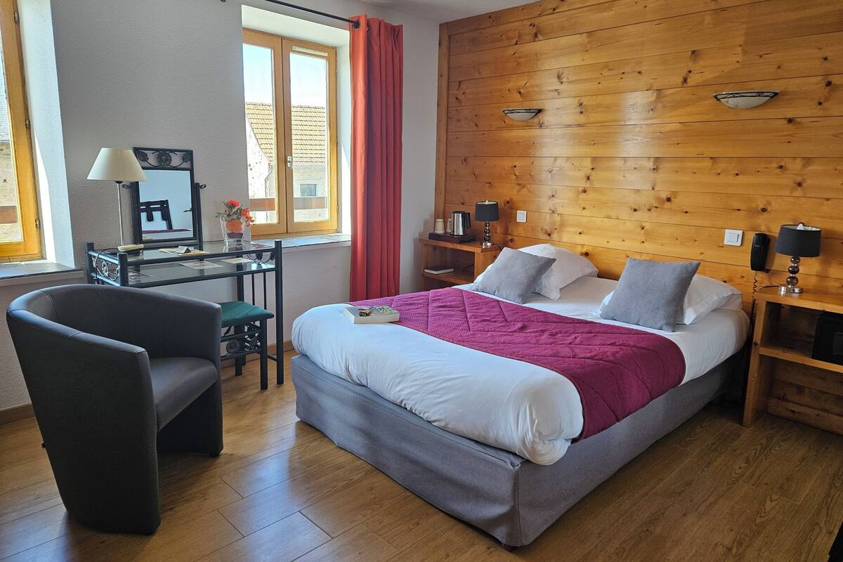 Ein Schlafzimmer mit Bett, Schreibtisch, Stuhl und einem Fenster mit Vorhängen.