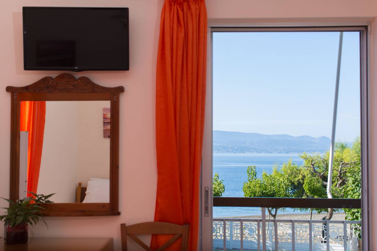 A room with a large mirror, a television mounted on the wall, and a view of a body of water through a balcony door.