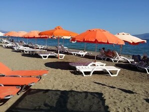 A beach with rows of white lounge chairs and orange umbrellas. - Pansion Akrogiali (Eretria)