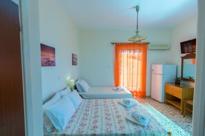 Ein Schlafzimmer mit zwei Betten, einem Schreibtisch, einem Stuhl, einem Kühlschrank und einem Deckenventilator.