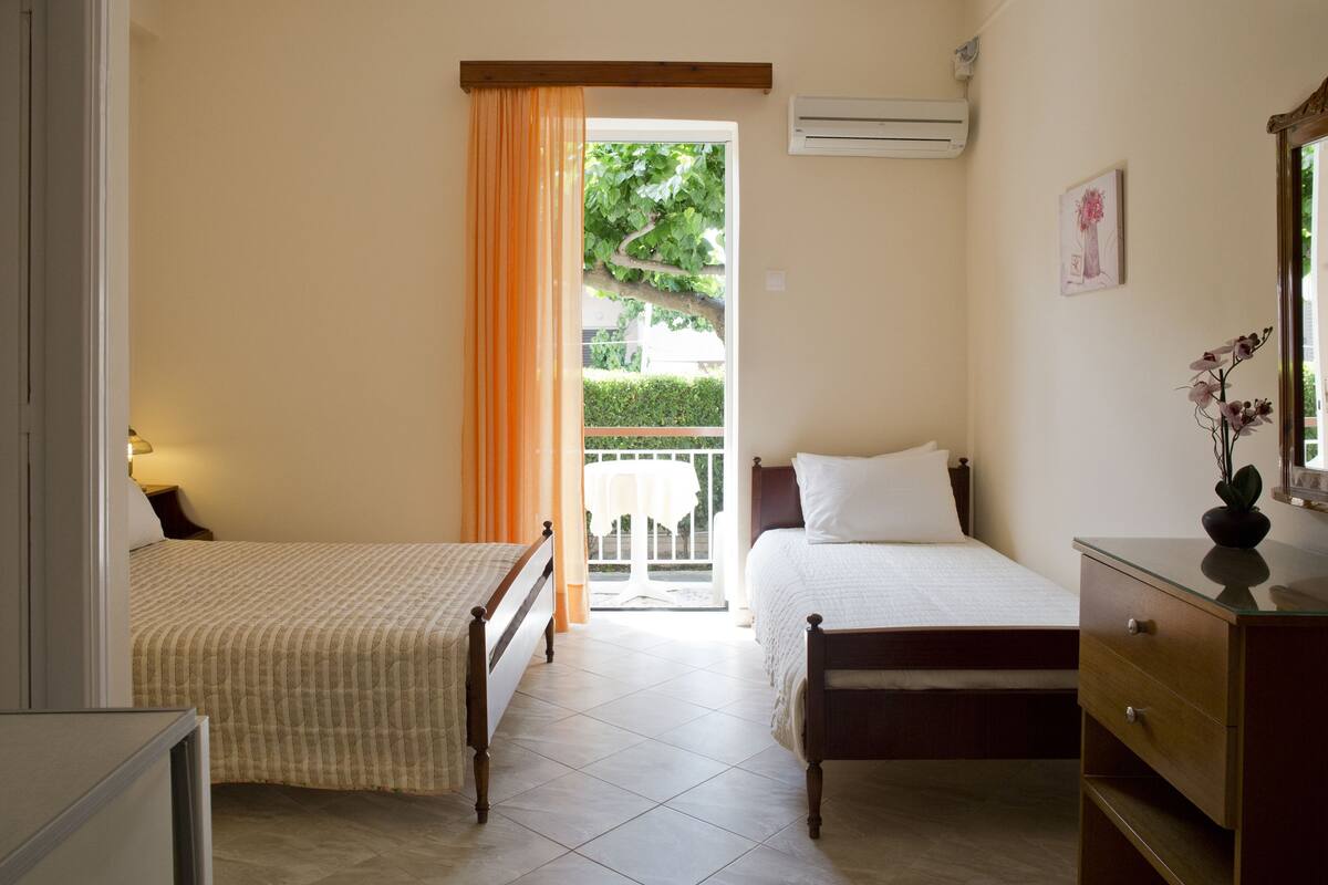 A bedroom with two beds, a dresser, an air conditioner, and a window with curtains.