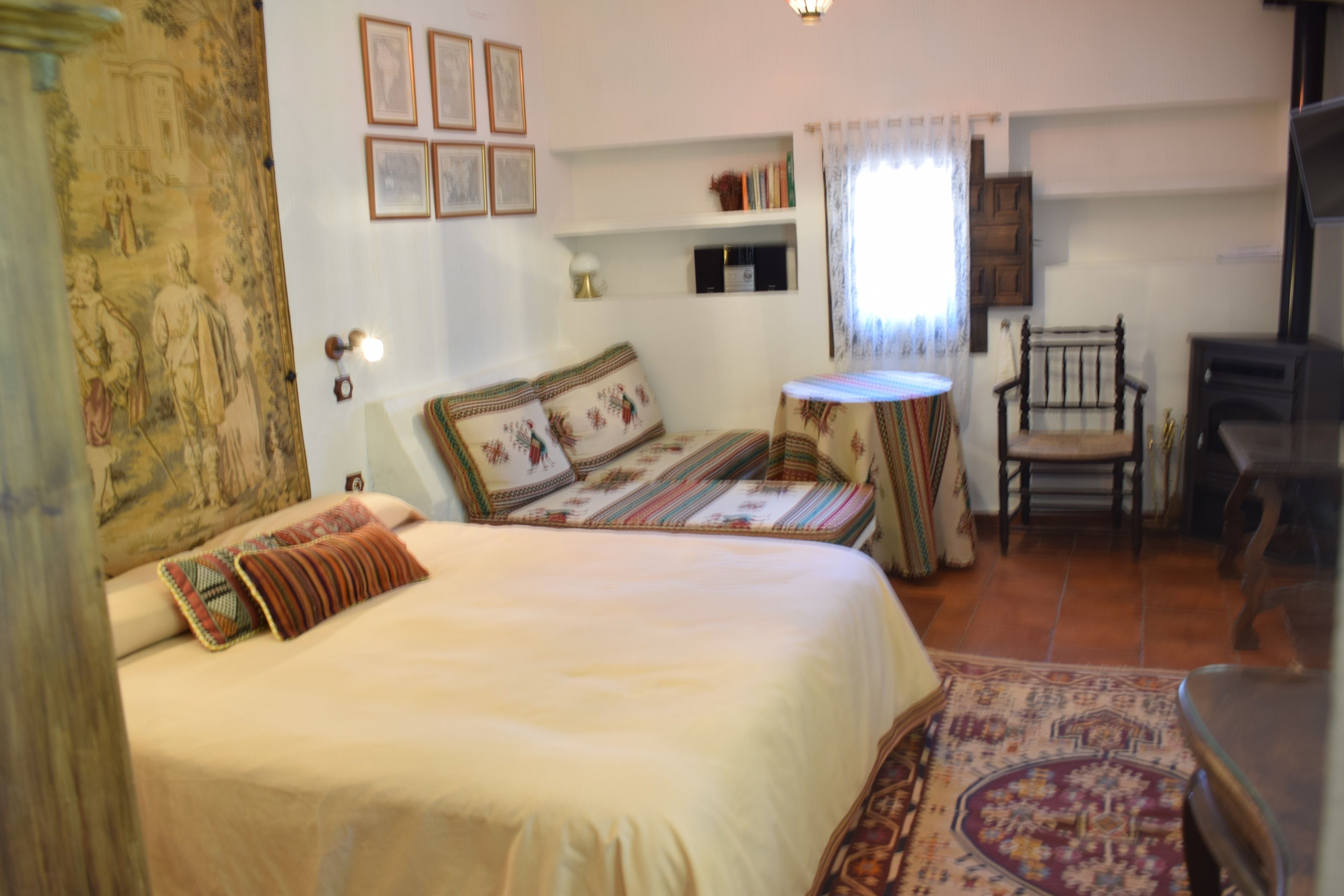 Une chambre à coucher comprenant un lit, une chaise, une petite table et une étagère avec des livres et des objets décoratifs.