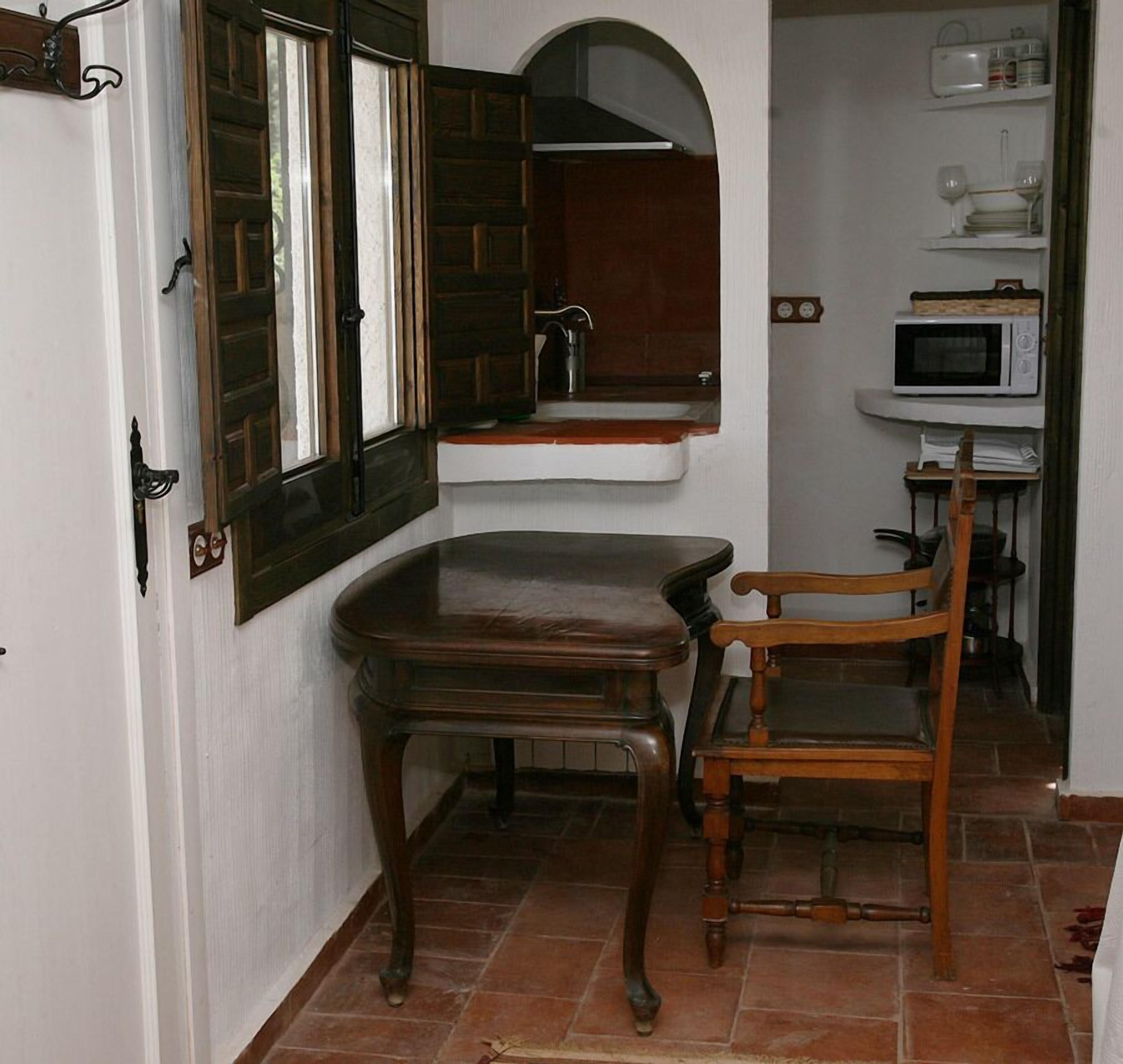 Un pasillo estrecho con una mesa y una silla de madera, un lavamanos y un microondas.