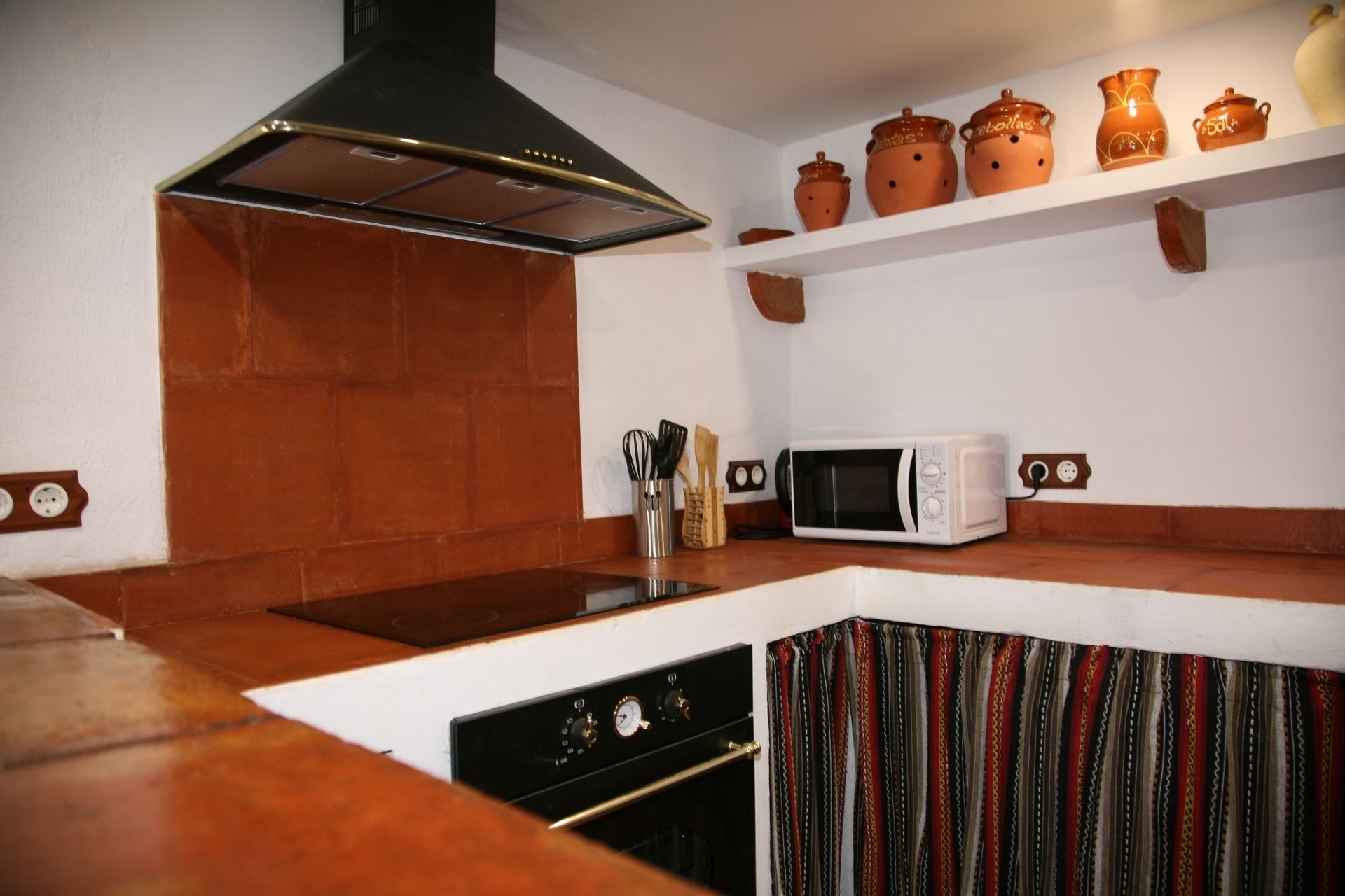 Una cocina con estufa, microondas y un estante con cerámica.