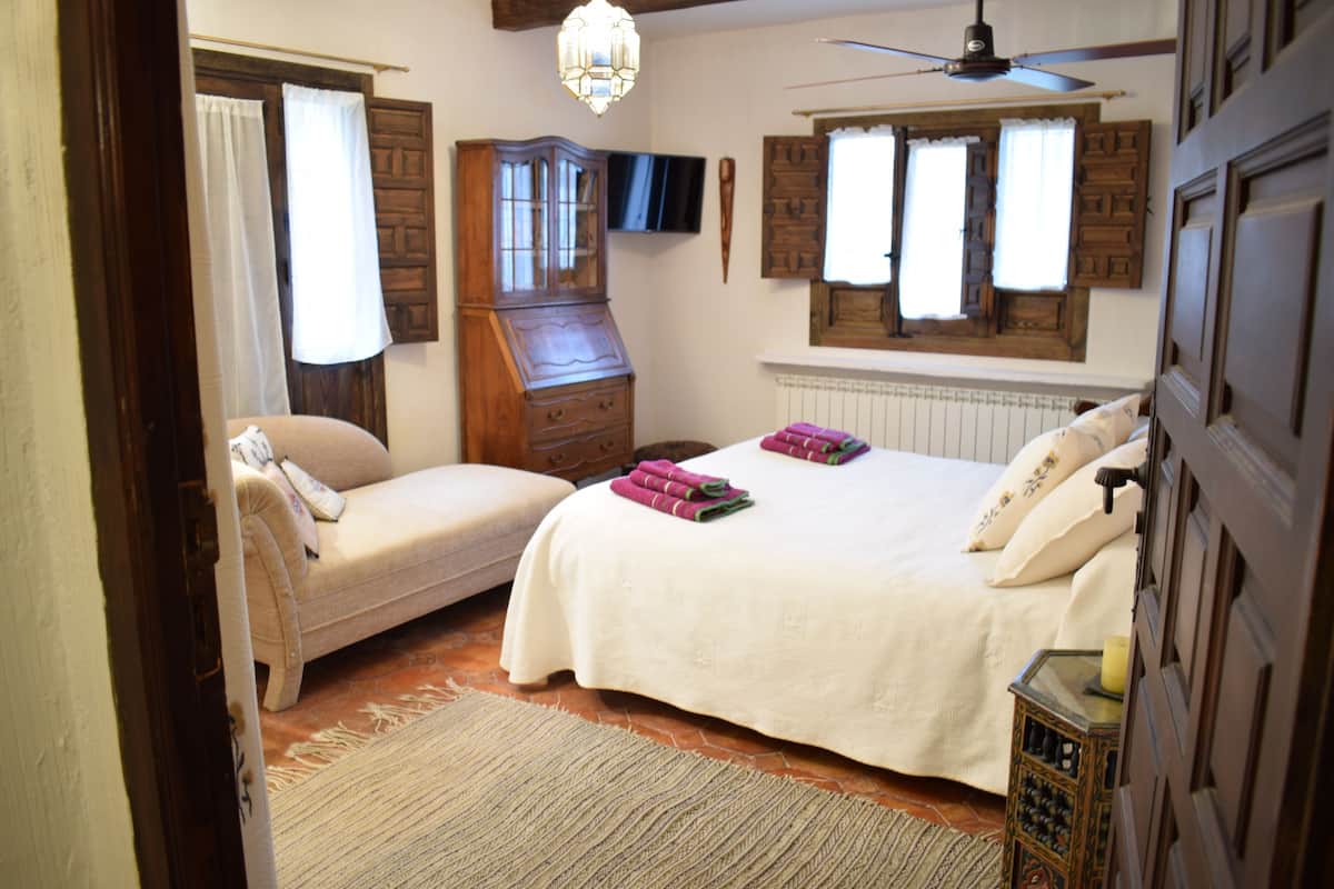 Ein Schlafzimmer mit Bett, einem Sessel, einem Holzschrank, einem Deckenventilator und einem Fernseher an der Wand.