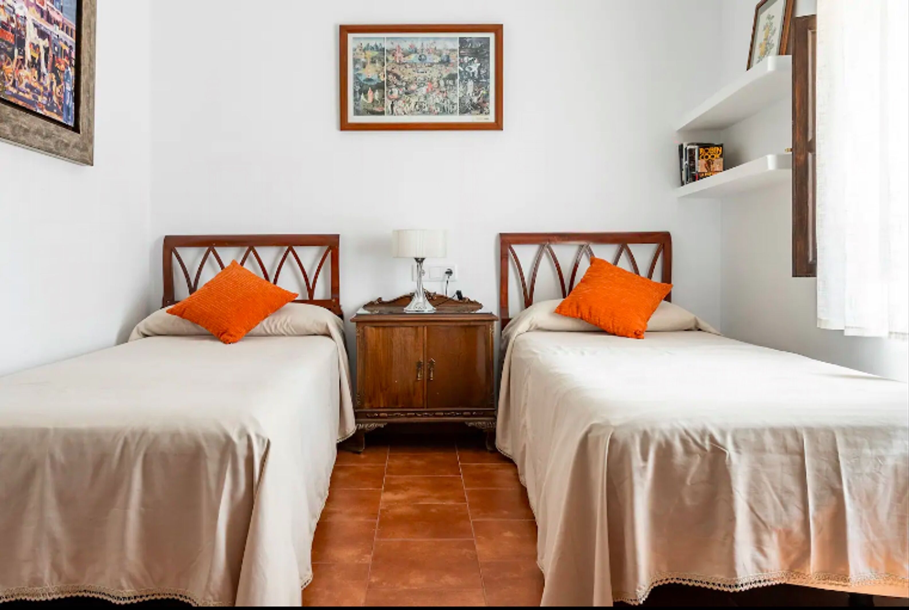 A room with two beds, a wooden nightstand, a lamp, and a painting on the wall.