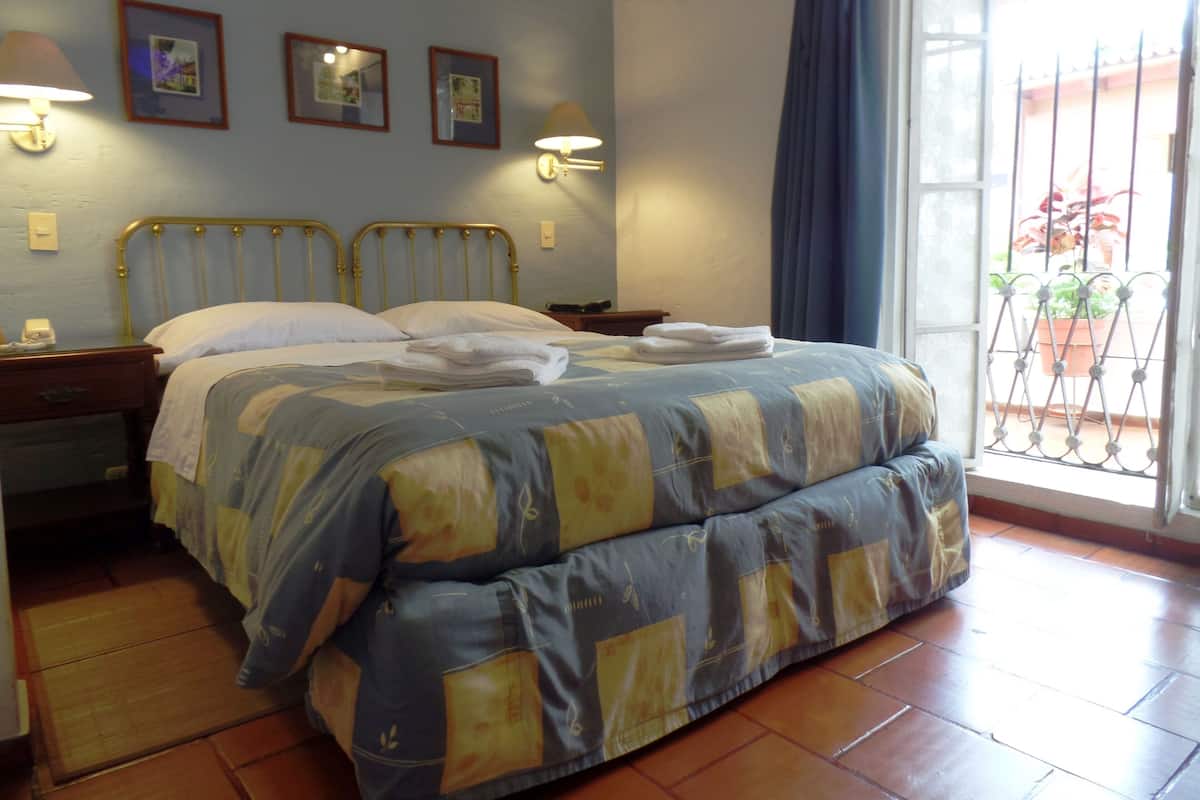 Een netjes opgemaakt bed met een beddekleed met patroon, twee bedlampjes en een raam met uitzicht.
