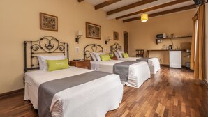 Habitación de hotel con dos camas, pisos de madera, kitchenette y obras de arte en las paredes.
