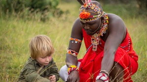 A person in traditional attire sitting in a grassy field.