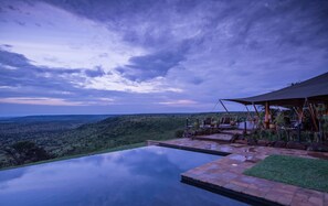 An infinity pool with a view of a hilly landscape and a covered outdoor seating area with chairs and tables. - Elewana Loisaba Tented Camp (Loisaba)