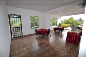 A spacious room with wooden flooring, two round tables with red tablecloths, and large windows offering views of greenery. - A&B events (Matale)