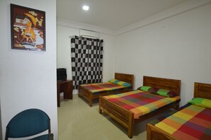 A room with three wooden beds, each with colorful bedding, a desk with a chair, and a painting on the wall. - A&B events (Matale)