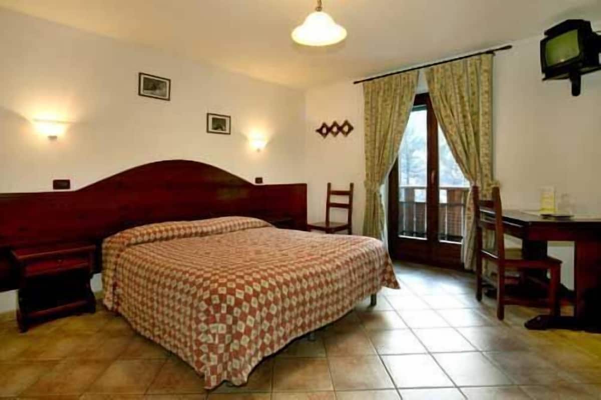 A hotel room with a large bed, a desk, a chair, a television, and a window with curtains.