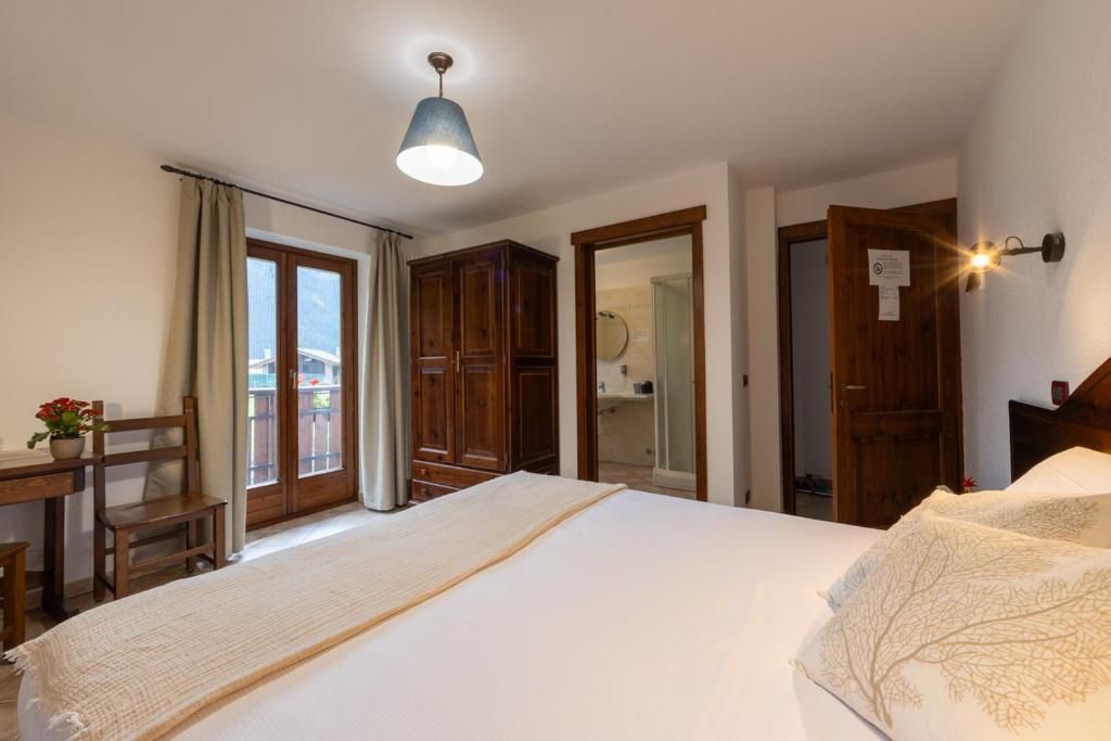 A bedroom with a bed, a desk, and a chair. There is a window with curtains, a door, and a wall-mounted light fixture.