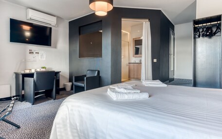 A modern hotel room with a large bed, a desk, a chair, and a TV mounted on the wall.