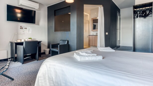 Une chambre d’hôtel moderne, dotée d’un grand lit, d’un bureau, d’une chaise et d’un téléviseur fixé au mur.