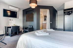 Una habitación de hotel moderna con una cama grande, un escritorio, una silla y un televisor montado en la pared.