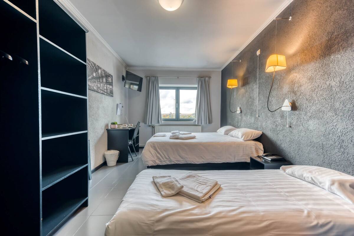 Habitación de hotel con dos camas, un escritorio, una silla, un televisor y una ventana con cortinas.