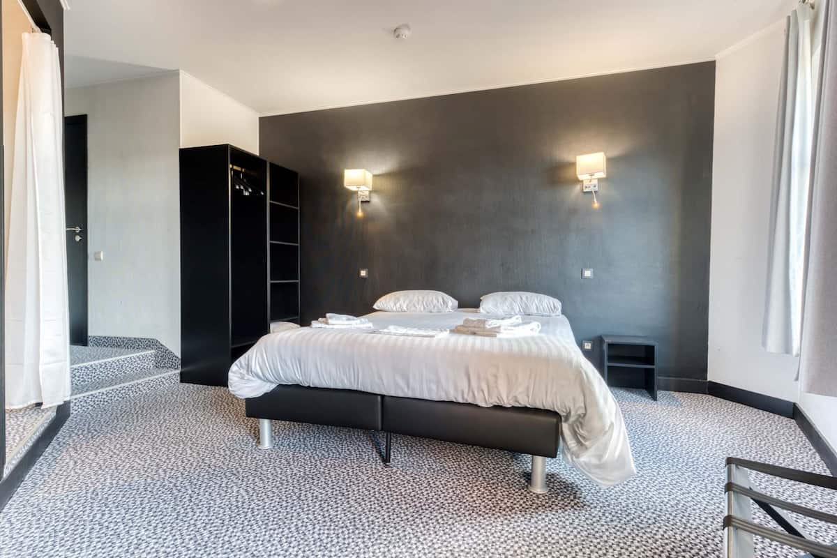 Un dormitorio moderno con una cama grande, dos lámparas de noche, una pared de acento oscura y una alfombra estampada.