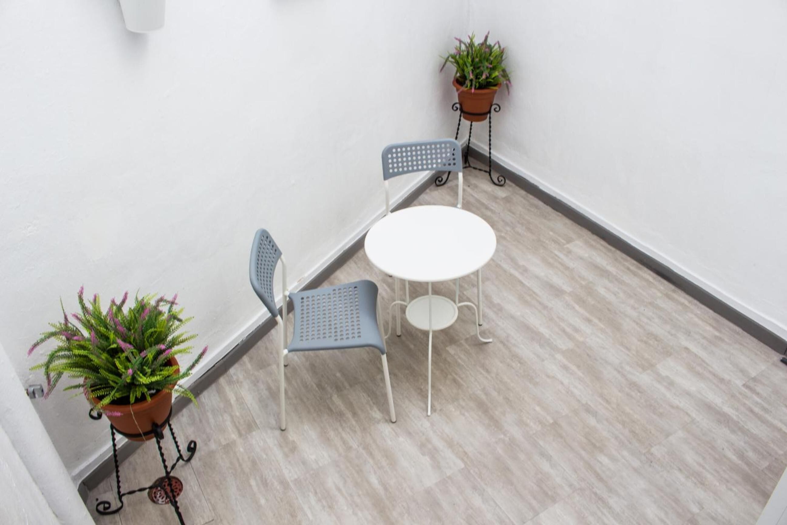 Un petit balcon avec deux chaises et une table, entouré de murs blancs et d’un plancher de couleur claire.