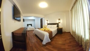 A hotel room with a bed, bedside tables, a desk, a TV, and a bathroom visible through an archway. - La Cabaña Hotel (Cusco)