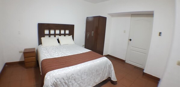 Un dormitorio con cama, armario, mesita de noche y puerta.