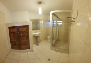 Une salle de bain avec une porte en bois, un lavabo, des toilettes et une douche séparée par une paroi de verre.