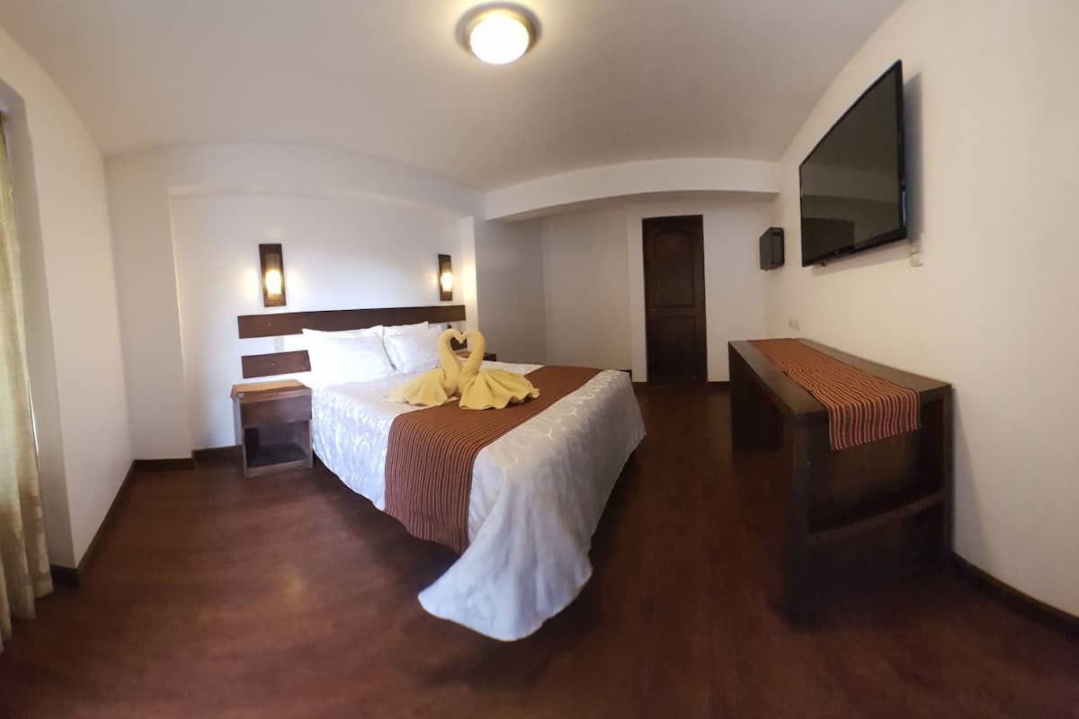 A hotel room with a bed, bedside tables, a TV, and a door.